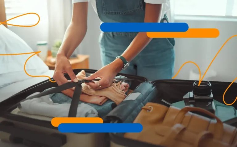 Manos terminando de hacer una maleta con ropa, bolso y cámara, destacando la importancia de los seguros de viajes para un viaje seguro