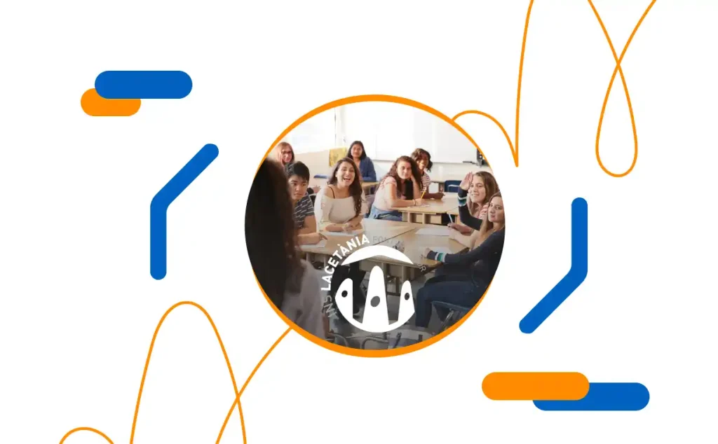 Grupo de estudiantes en un aula del Instituto Lacetània atendiendo a una profesora, con el logotipo del instituto en el centro de la imagen
