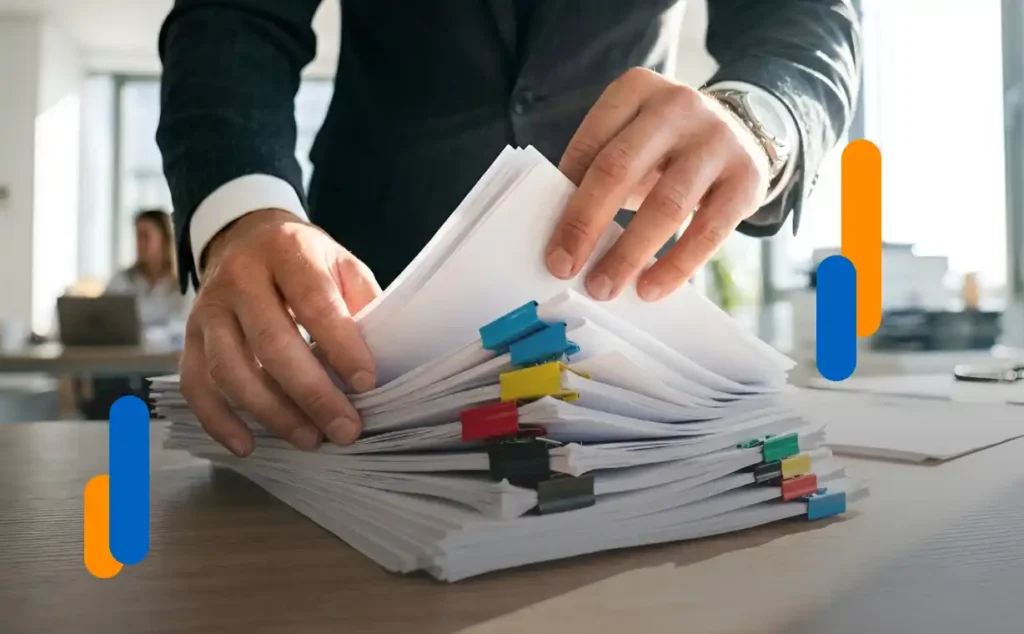 An executive sorting through a large stack of paper documents held together with colored paper clips—a clear example of the bureaucracy that can be avoided to achieve a frictionless hiring process